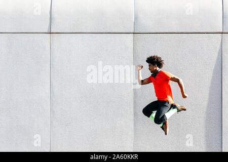 Young man doing jumps with a gray wall in the background Stock Photo