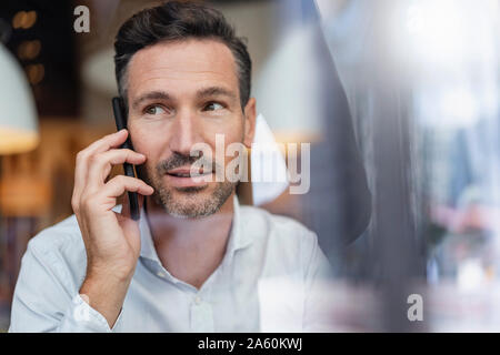 Portrait of businessman on the phone behind windowpane in a cafe Stock Photo