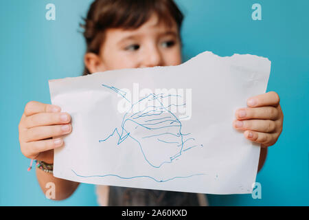 Little girl holding a handmade drawing on blue background Stock Photo