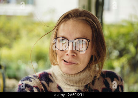 Portrait of young woman with glasses wearing fluffy sweater blowing up a strand of hair Stock Photo