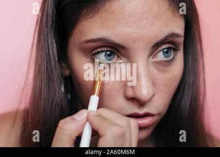 Close up of a young brunette woman with beautiful blue eyes applying eyeshadow with an eye brush Stock Photo