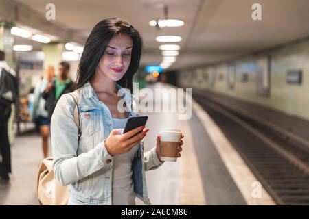 Young woman with cell phone at metro station waiting for the train, Berlin, Germany Stock Photo