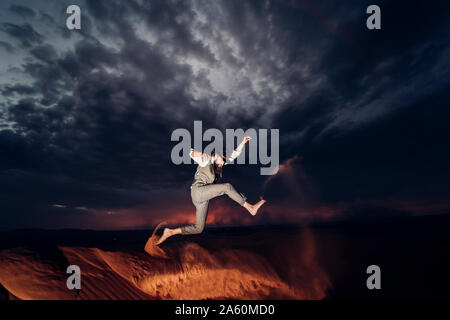 Man with a beard and hat jumping in the dunes of the desert of Morocco at dusk Stock Photo