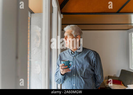 Serious senior man looking at home through window Stock Photo