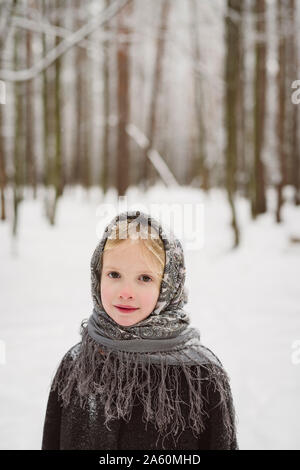 Portrait of little girl wearing headscarf standing in front of winter forest Stock Photo