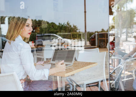 Young woman with laptop on table in a cafe looking out of window