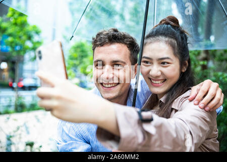 Happy couple with umbrella taking a selfie in Ginza, Tokyo, Japan Stock Photo