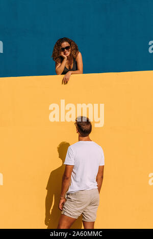 Young man looking at woman behind a yellow wall Stock Photo