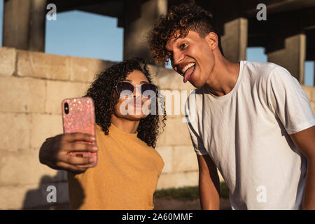 Young couple taking selfies with smartphone, sitting in front of wall Stock Photo