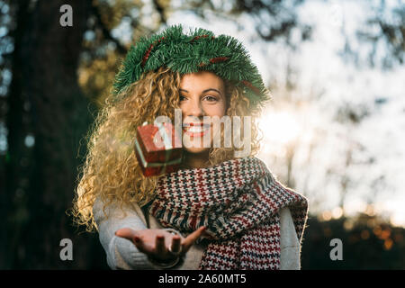 Portrait of smiling young woman with Christmas wreath on her head juggling with Christmas present Stock Photo
