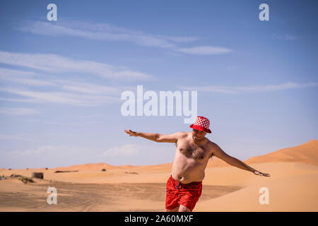 Happy overweight man with swimming shorts running in the desert of Morocco Stock Photo