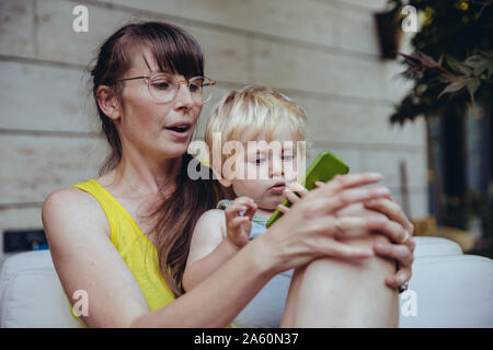 Little boy sitting on mother's lap, looking at smartphone Stock Photo