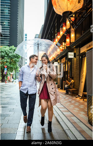 Happy couple with umbrella walking in Ginza, Tokyo, Japan Stock Photo