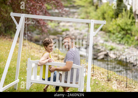 Portrait of smiling couple sitting on canopy swing in garden Stock Photo