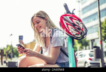 Smiling young woman with E-Scooter looking at cell phone, Berlin, Germany Stock Photo