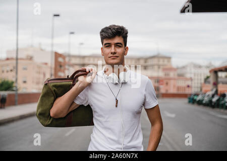 Young man with a bag at train station wearing headphones