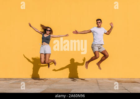 Young couple jumping in front of a yellow wall Stock Photo