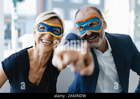 Businessman and woman wearing super hero masks, pointing at camera Stock Photo