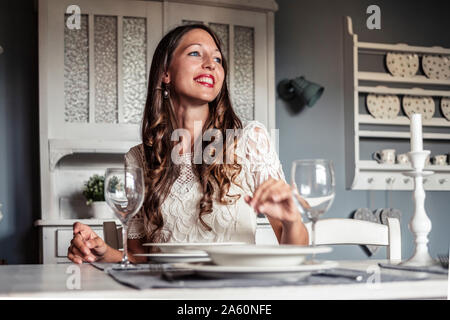 Portrait of smiling young woman sitting at laid table in country style kitchen Stock Photo