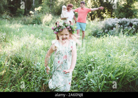 Happy little girl with flower wreath running from her parents in nature Stock Photo