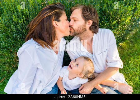 Parents kissing with little daughter watching Stock Photo