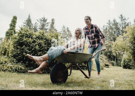 Daughter pushing mother, sitting in push cart, through the garden Stock Photo