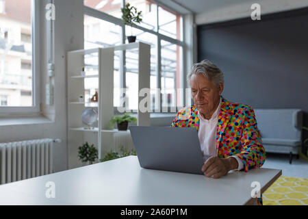 Senior businessman wearing colorful sports jacket using laptop Stock Photo