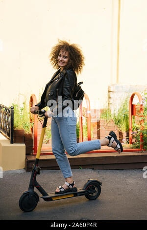 Portrait of smiling teenage girl standing on scooter Stock Photo