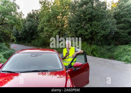 Senior man standing at his broken car using his smartphone Stock Photo