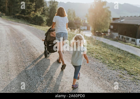 Mother with daughter, stroller and dog walking on forest path Stock Photo