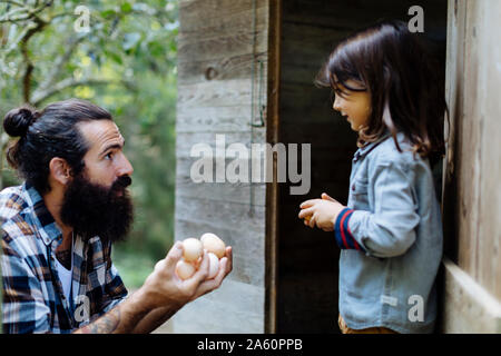 Father and kid collecting eggs at chicken coop on an organic farm Stock Photo
