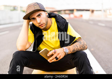 Portrait of tattooed young man with smartphone wearing baseball cap Stock Photo