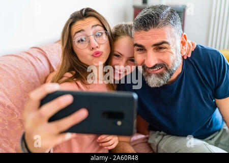 Happy father with two daughters taking selfie on couch at home Stock Photo