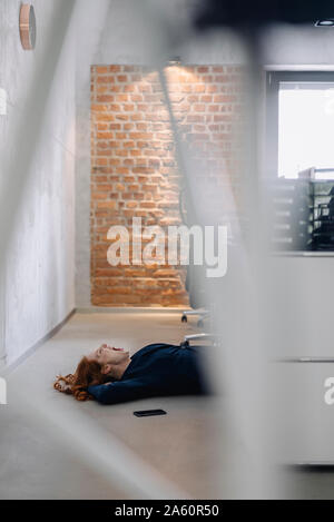 Tired businesswoman lying on the floor in office Stock Photo