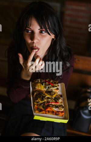 Young girl in the city eating a piece of pizza at night Stock Photo