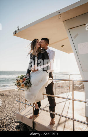 Happy bride and groom at lifeguard hut on the beach at sunset Stock Photo