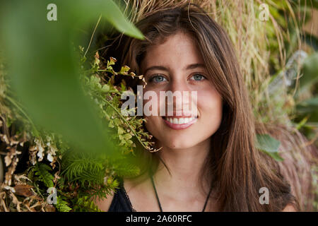 Portrait of smiling young woman in front of plant wall Stock Photo