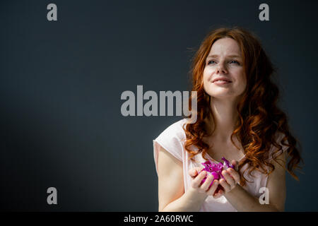 Portrait of redheaded woman with hadful of purple orchid blossoms Stock Photo