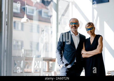 Businessman and woman wearing super hero masks, standing in coffee shop Stock Photo