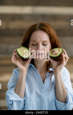 Portrait of redheaded woman with eyes closed holding sliced avocado Stock Photo