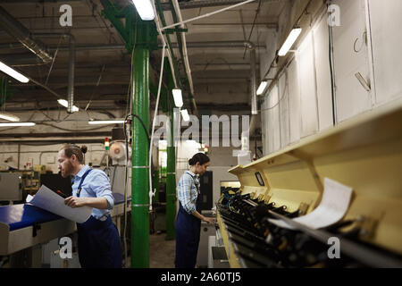 Manual workers in overalls working on lathes for printing papers in the printing plant Stock Photo