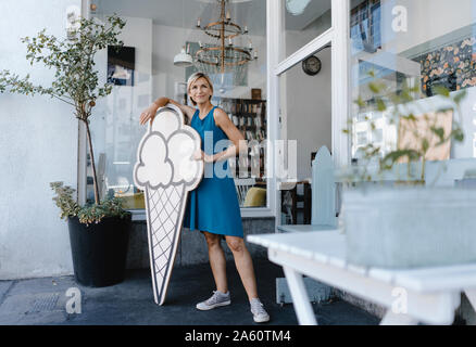 Woman standing in front of her coffee shop, holding icecream sign Stock Photo