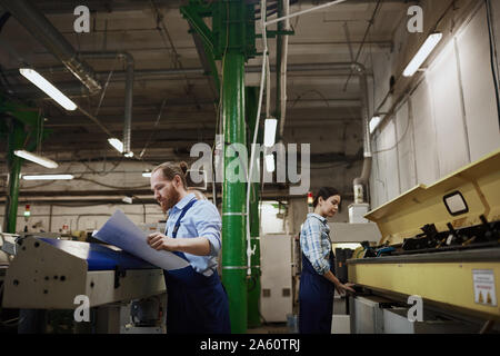 Two manual workers in overalls busy with their work on lathes in printing plant Stock Photo