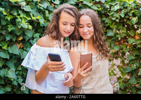 Young girls using smartphone on ivy background Stock Photo