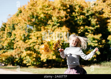 Portrait of smiling little girl running with autumn wreath in the park Stock Photo
