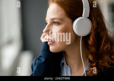 Portrait of redheaded businesswoman listening music with white headphones Stock Photo