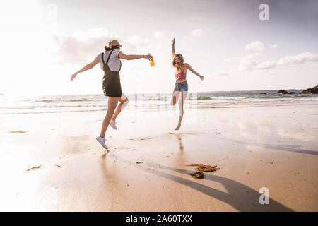 Two girlfriends having fun, running and jumping on the beach Stock Photo