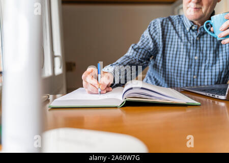 Senior man sitting at home in front of laptop making notes Stock Photo