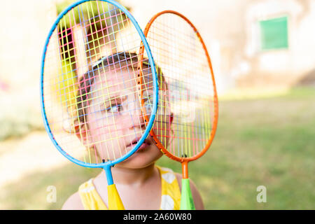 Little girl playing with colorful badminton rackets outdoors in summer