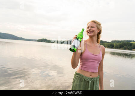 Happy young woman drinking water at a lake Stock Photo